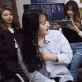 a group of young women are sitting in a room . one of the girls is holding a tablet .