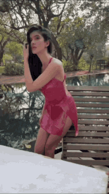 a woman in a pink dress is standing on a wooden bench near a pool