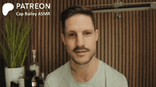 a man with a beard is smiling in front of a sign that says patreon cap bailey asmr
