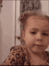 a little girl wearing a leopard print shirt is making a face .