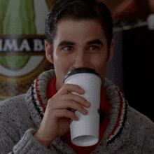 a man drinking a cup of coffee in front of a sign that says ' imab '