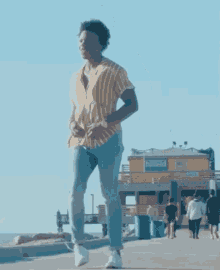 a man in a yellow striped shirt and blue jeans is walking on a beach .