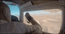 a man is looking out the window of an airplane with 4gifs.com written on the bottom right
