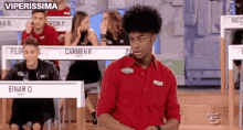 a man in a red shirt is sitting in front of a table with the name carmen f. on it