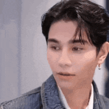 a young man wearing a denim jacket and earrings looks at the camera .