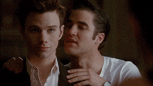 a man in a white shirt is whispering into the ear of another man in a black suit