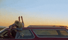 a woman is laying on the roof of a car at sunset
