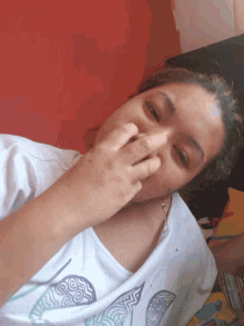 a woman covering her nose with her hand while wearing a white shirt with seashells