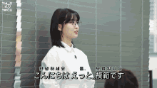 a woman wearing glasses and a white shirt stands in front of a wall with a twice logo on it