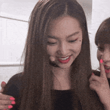 a woman with a microphone on her head smiles while another woman holds her finger to her mouth