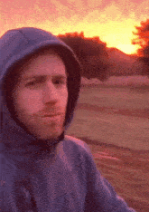 a man wearing a hooded jacket is standing in front of a sunset