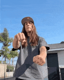 a man with long hair is wearing a hat and a gray shirt .