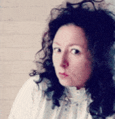 a woman with curly hair wearing a white shirt looks at the camera