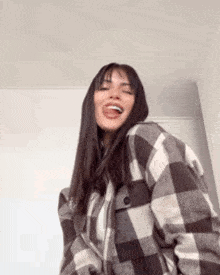 a woman wearing a plaid jacket is laughing and sticking her tongue out .
