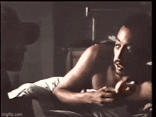 a man without a shirt is laying in bed with a cigarette in his mouth .