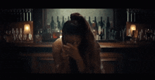 a woman sitting at a bar covering her eyes with her hands