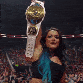 a woman holds up a wrestling championship belt in front of a crowd with raw signs in the background
