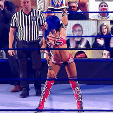 a woman in a wrestling ring is holding a championship belt while a referee looks on .