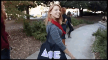 a woman is walking down a sidewalk with a bag that has the letter ae on it