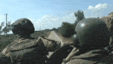 two soldiers wearing green helmets are looking out over a dirt road
