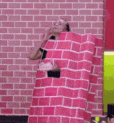 a woman in a pink brick costume is standing in front of a pink brick wall .