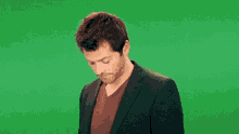 a man in a suit and a red shirt is looking down on a green screen .