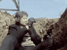 a man is sitting in the dirt with a gun