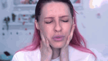 a woman with pink hair is holding her face with her hands