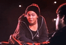 a woman wearing a black beanie is talking to a man in a dark room
