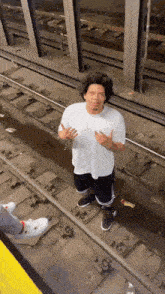 a man in a white shirt and black pants stands on train tracks