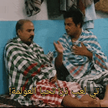two men wrapped in plaid blankets are sitting on a bed talking