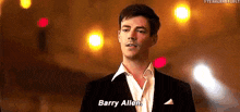 a man in a suit and white shirt is standing in front of a blurry background and talking to barry allen .
