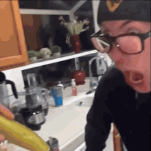 a man wearing glasses holds a banana in his mouth