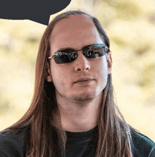 a man with long hair wearing sunglasses looks at the camera