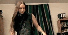 a man with long hair is standing in a room with a striped curtain .