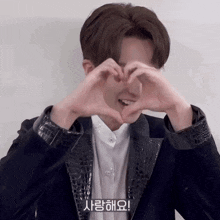 a man in a suit making a heart shape with his hands in front of his face in korean