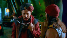 a man in a turban is holding a lamp and talking to another man in a red hat