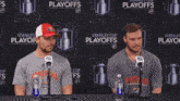 two men sitting at a table with microphones in front of a stanley cup playoffs wall