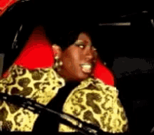 a woman in a leopard print jacket is sitting in a car with a red seat cushion .