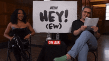 a man and woman sit in front of a sign that says hey ( ew )