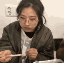 a woman is sitting at a table eating food with chopsticks .