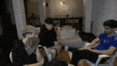 a man wearing a blue adidas shirt sits with two other men in a living room