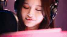 a young woman wearing headphones is looking at a pink tablet .