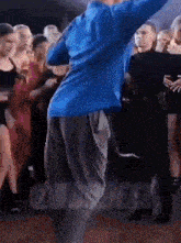 a man in a blue shirt is dancing in front of a crowd of people