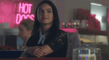 a woman sits at a table in front of a hot dog sign