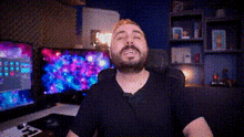 a man with a beard is sitting in a chair in front of a computer monitor .