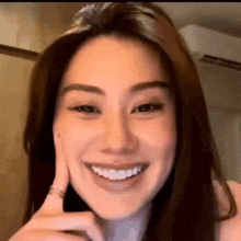 a close up of a woman 's face smiling with her hand on her chin .