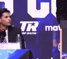 a man sits in front of a sign that says tr group rank
