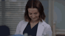 a woman in a white coat and blue scrubs is smiling .