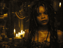 a woman with dreadlocks stands in a dark room with candles in the background and the letters w and y visible